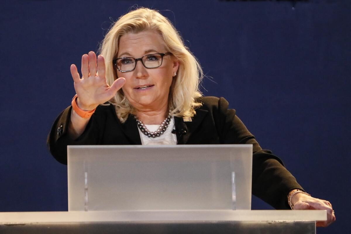 A woman stands behind a lectern, raising her arm halfway.