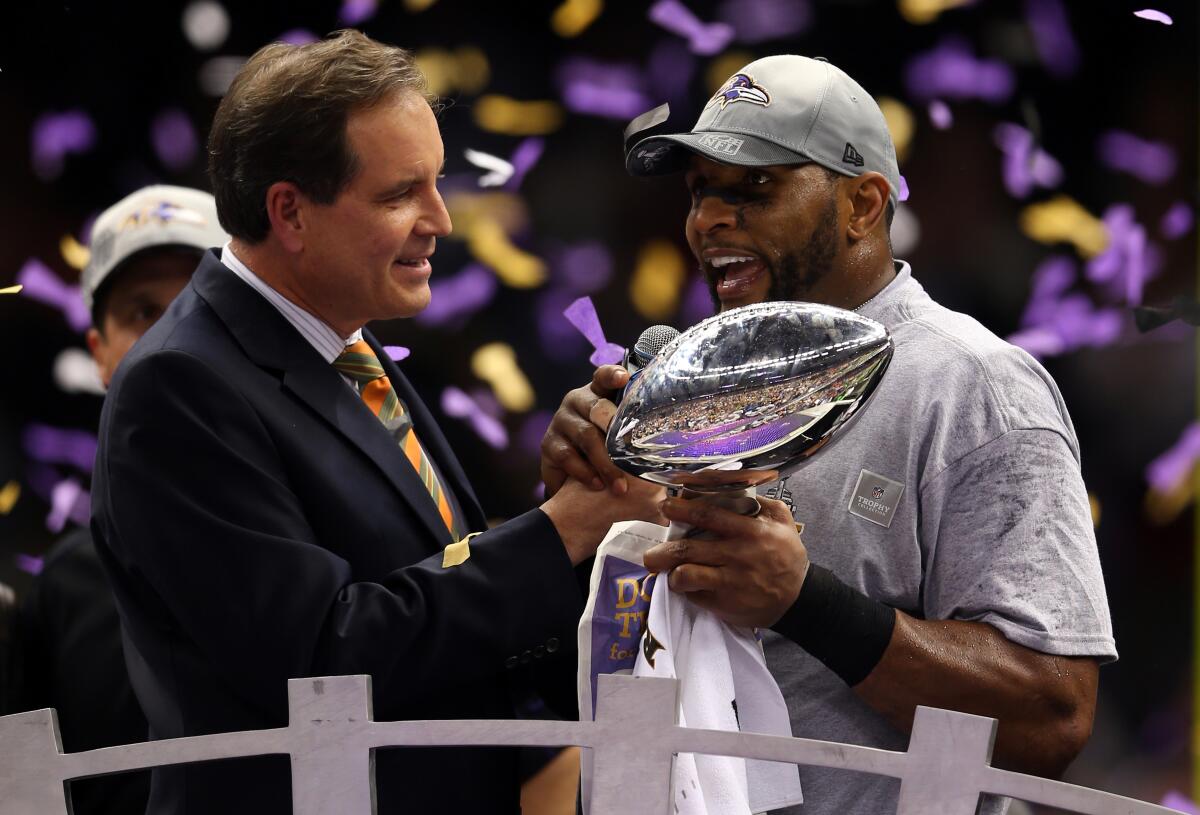 Jim Nantz holds the mic in front of Baltimore linebacker Ray Lewis while he holds a trophy.