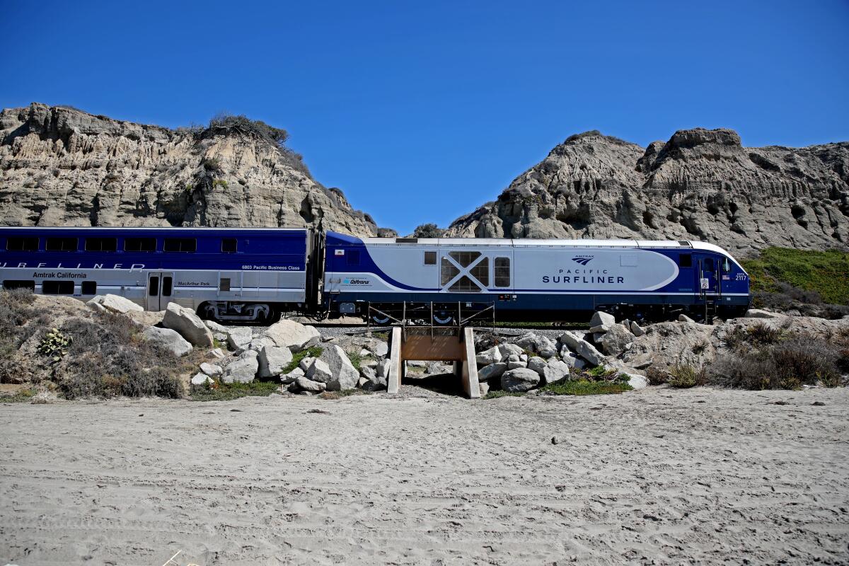 An Amtrak Surfliner train passing between hills and sand.