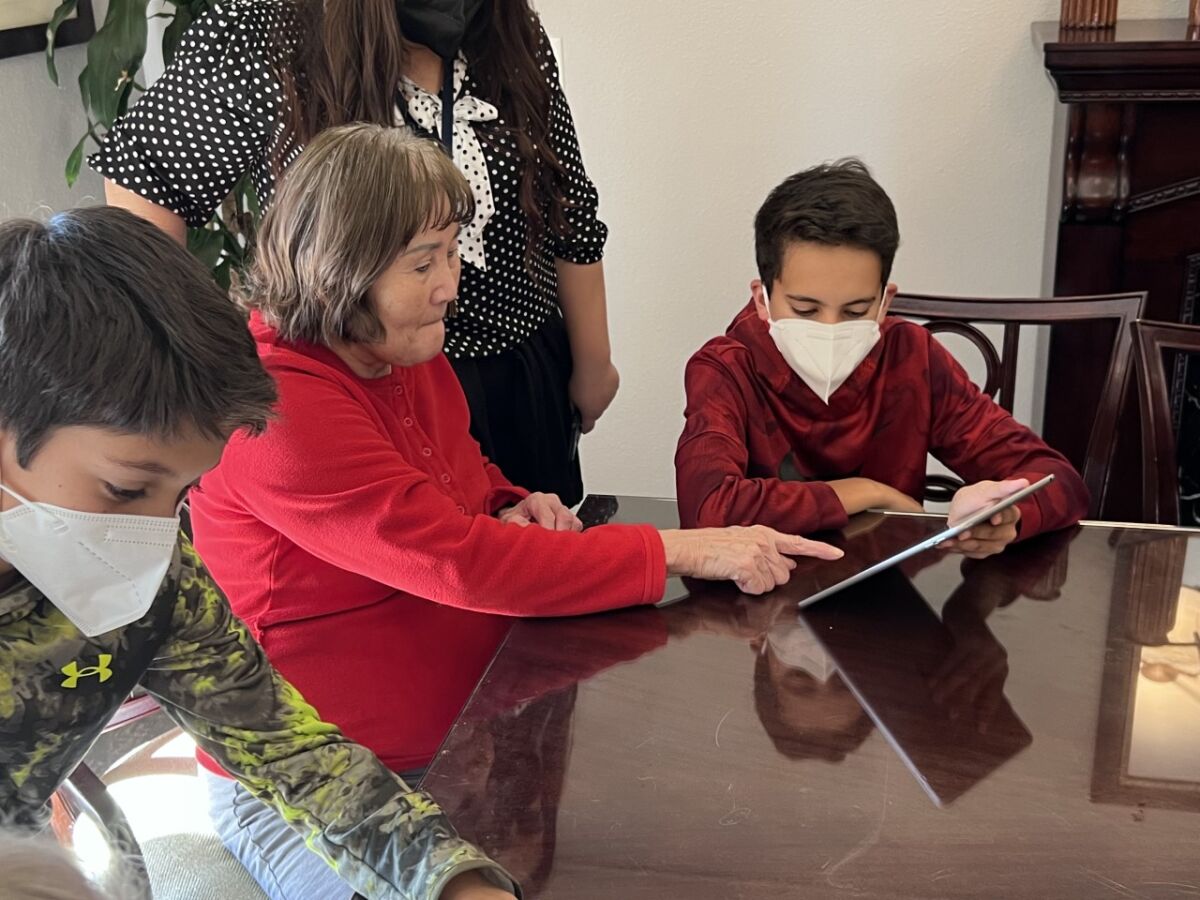 two boys sit with seniors at a table using iPads