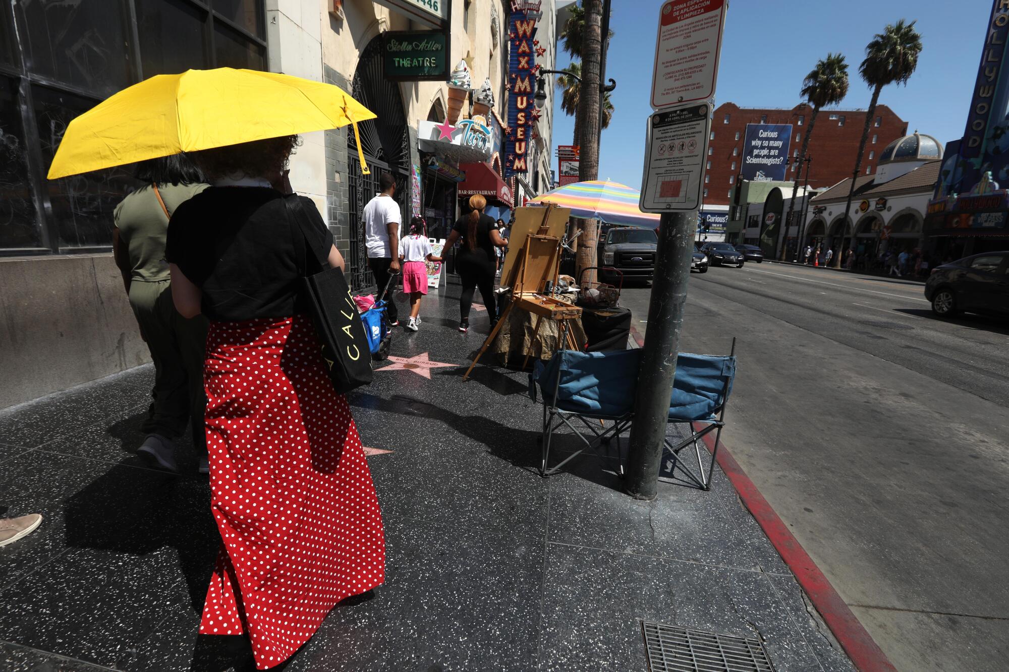 Woman with yellow umbrella walk along Hollywood Blvd.  