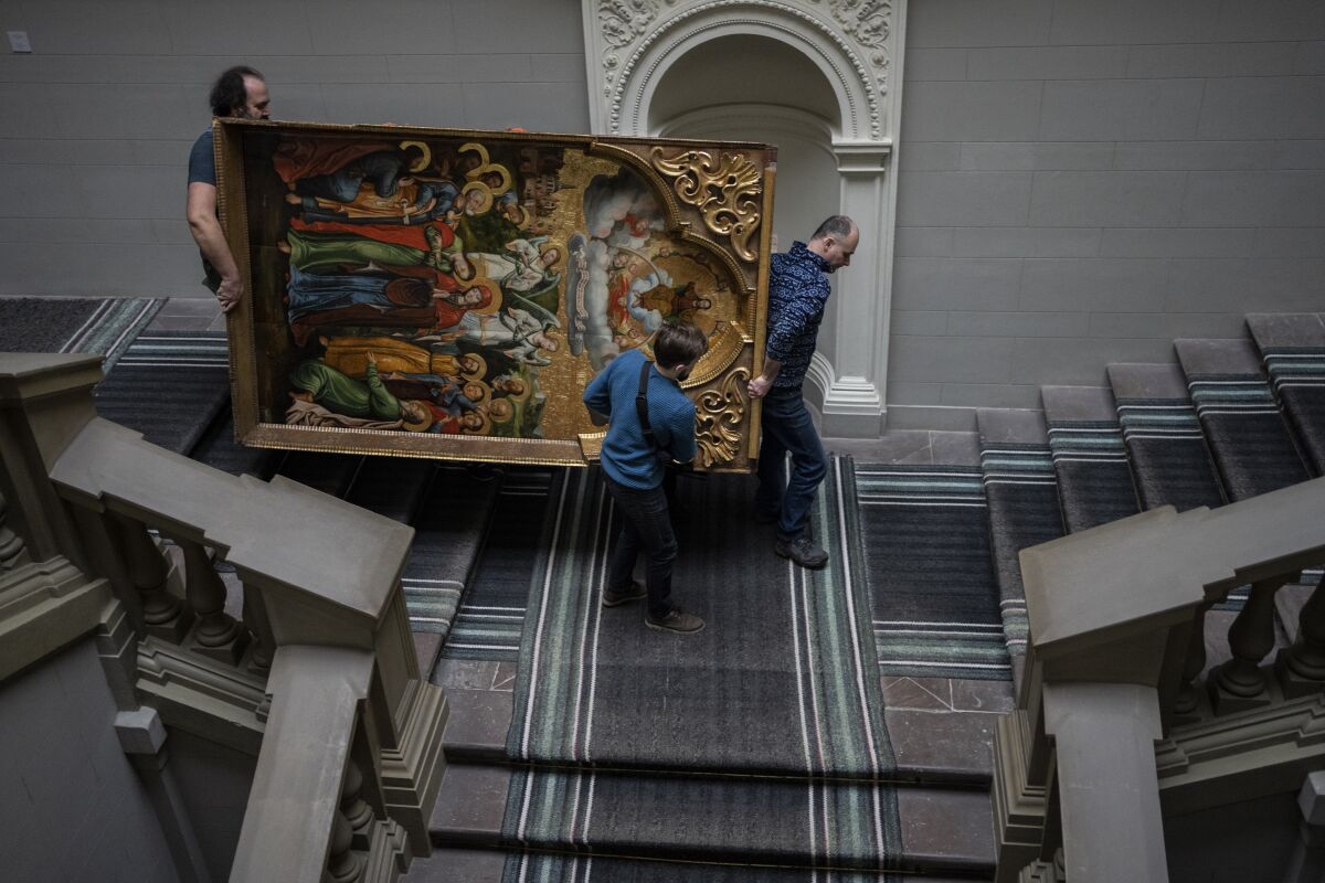Workers move a large painting of the Annunciation down a flight of stairs in a museum. 