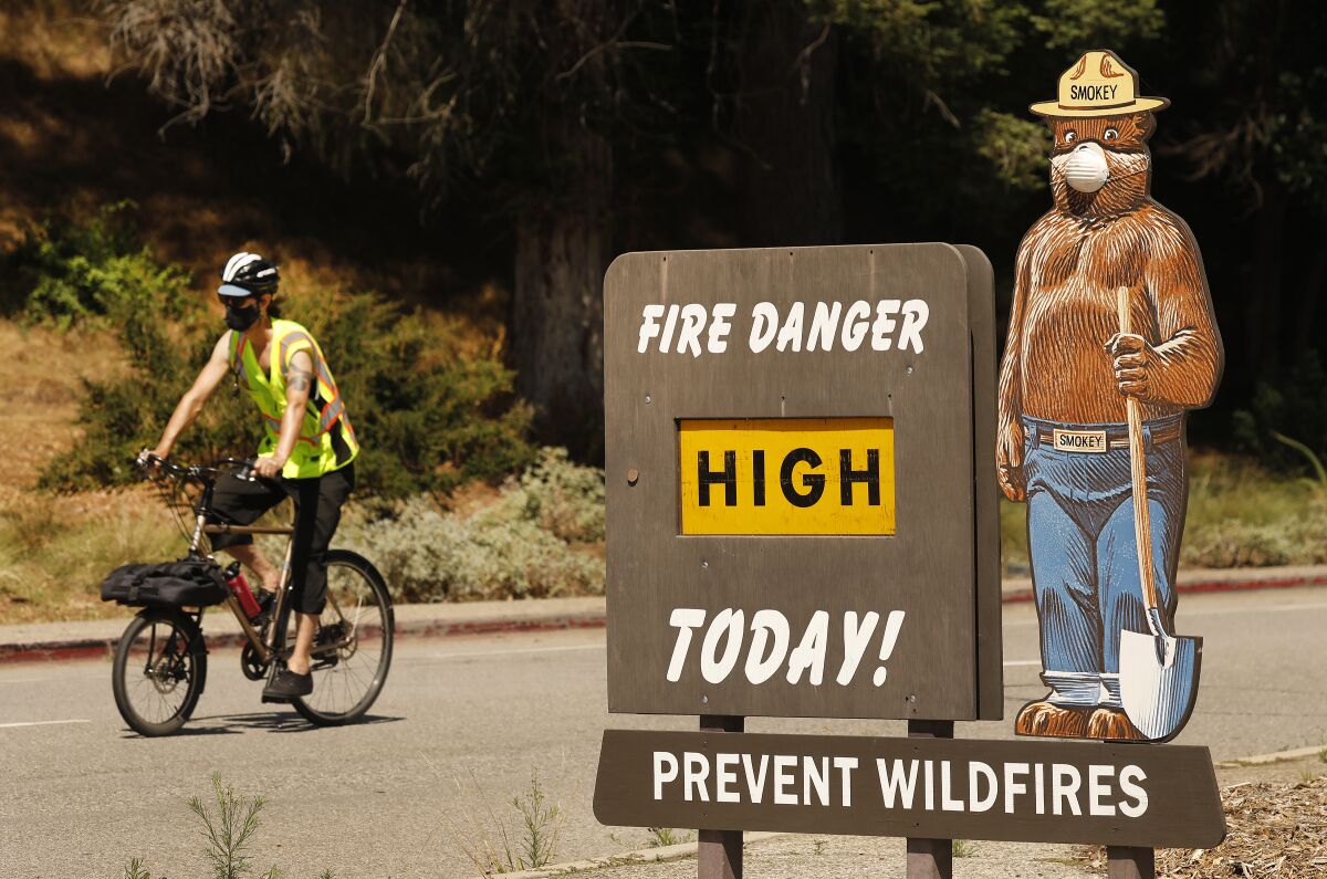A cyclist, left, passes a Smokey the Bear sign that says "Fire danger high today! Prevent wildfires"