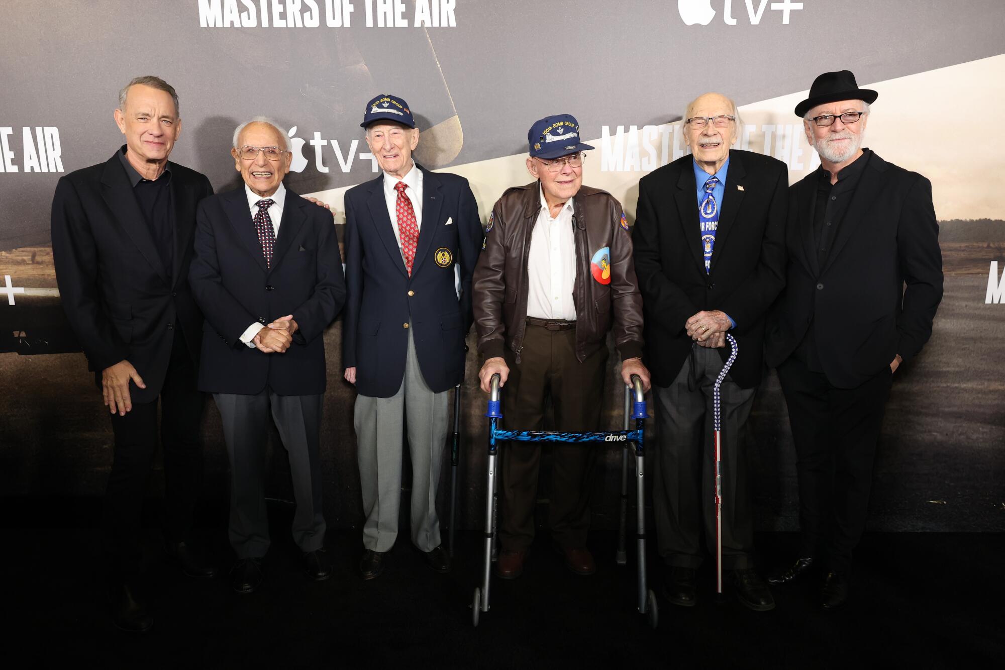 Six men, including one using a walker and another holding a cane, pose for photographs
