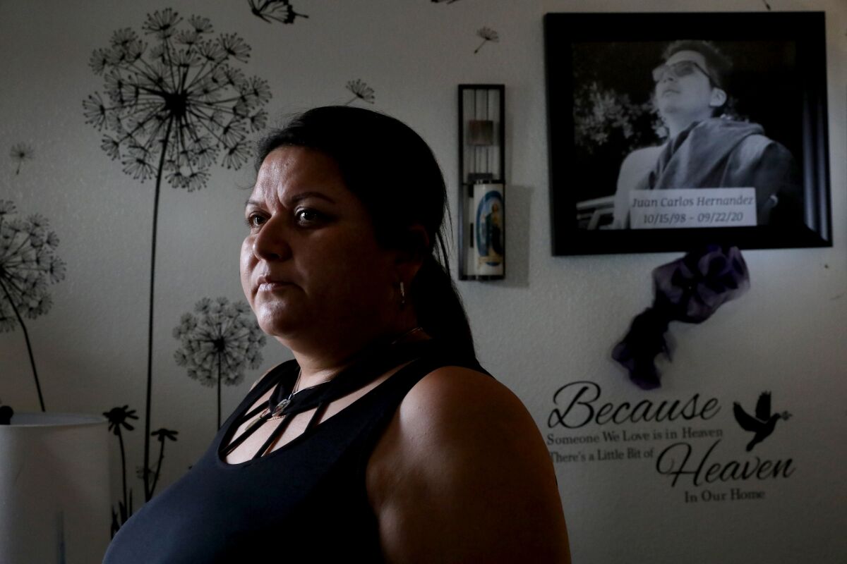 A woman in a home with a picture of her missing son on a wall behind her.
