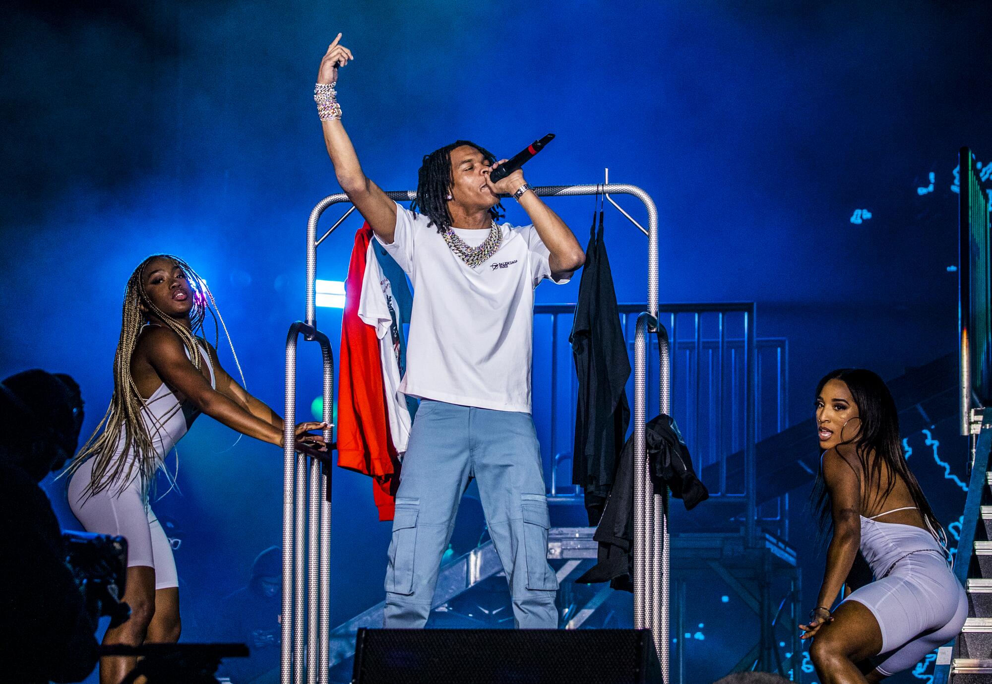 A man sings into a mic flanked by two women dancers