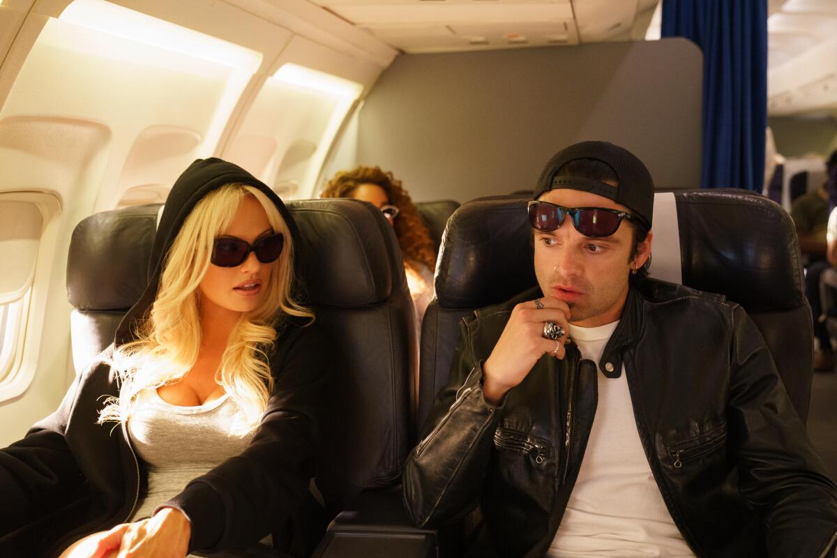 A man and woman in sunglasses sit on a plane in a scene from "Pam & Tommy."