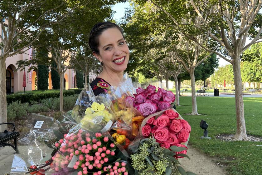 Floral designer Ana Galena poses at Liberty Station with arms full of flowers for her work.