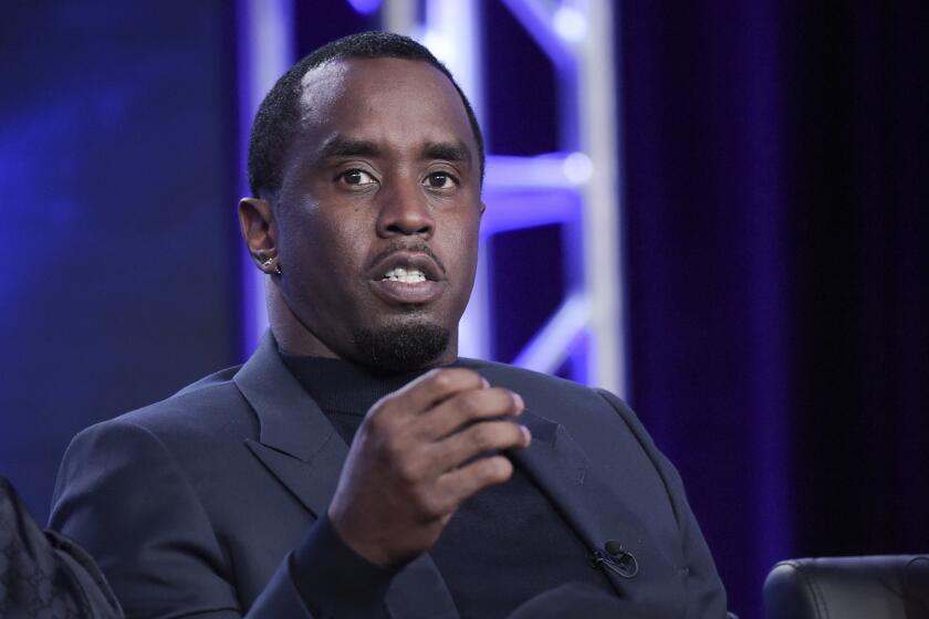 Sean 'Diddy' Combs is seated in a suit and motions with his right hand