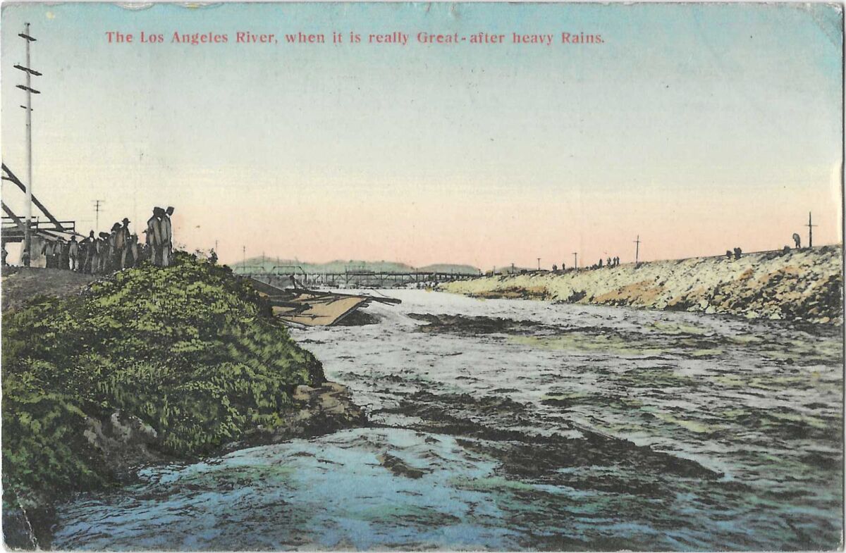 Water rushes in the L.A. River basin, with a bridge in the background and people on either bank