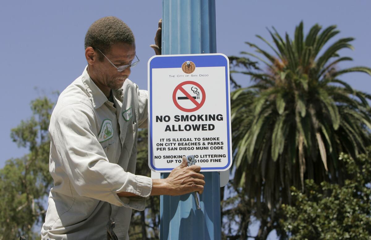 Tony Van of the San Diego Developed Regional Parks Division installs a "no smoking" sign on a light pole 