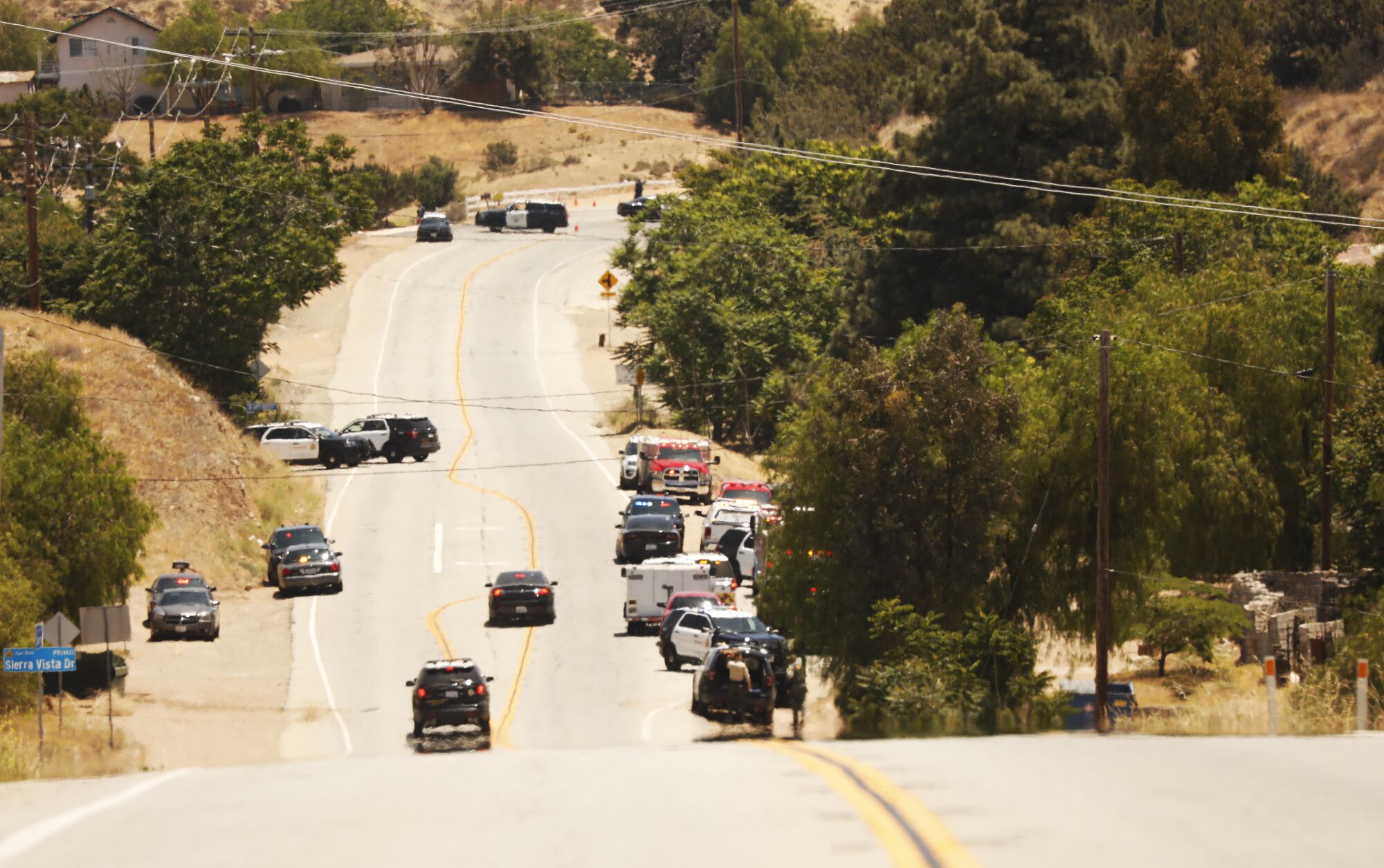 Emergency vehicles line a hilly road.