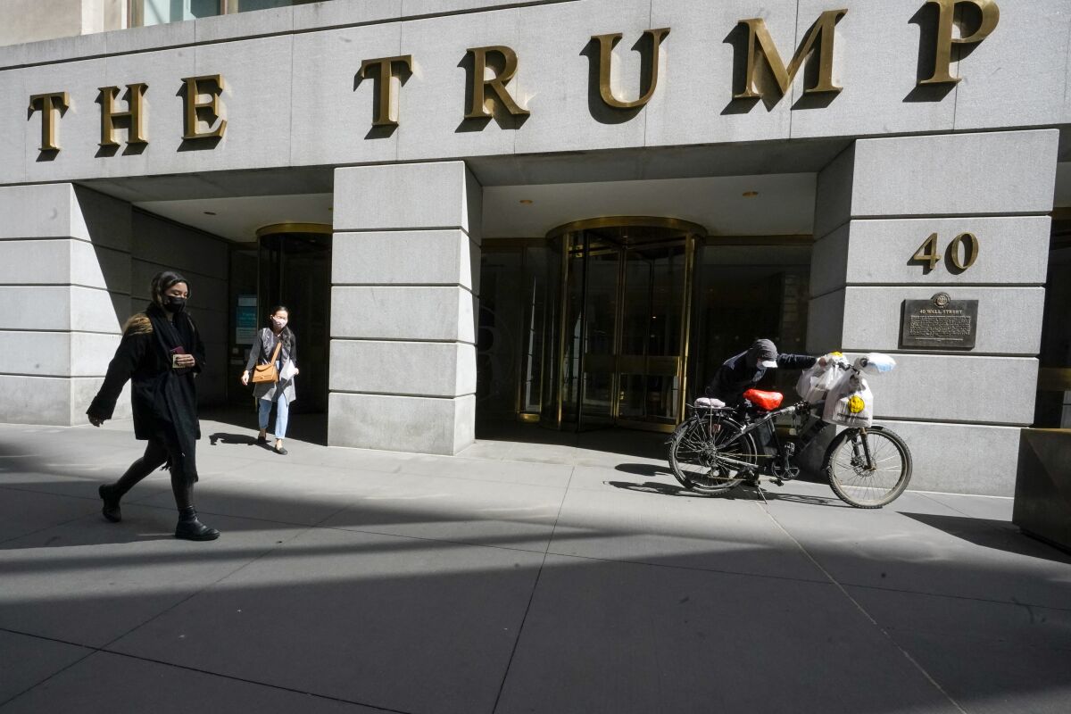 FILE - Pedestrians and a food delivery man are seen outside the Trump building at 40 Wall Street in New York's Financial District, Tuesday, March 23, 2021. The New York attorney general, Tuesday, Jan. 18, 2022, says her investigators have uncovered evidence that former President Donald Trump's company used "fraudulent or misleading" valuations of its golf clubs, skyscrapers and other property to get loans and tax benefits. (AP Photo/Mary Altaffer)