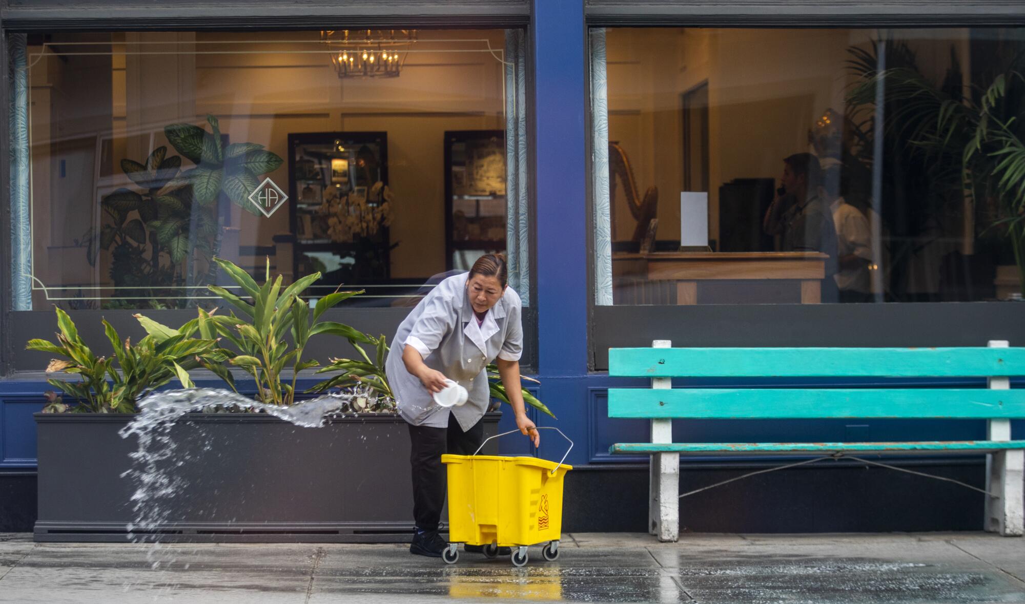 A woman carefully cleans the sidewalk outside the Hotel Atwater in Avalon, CA. 