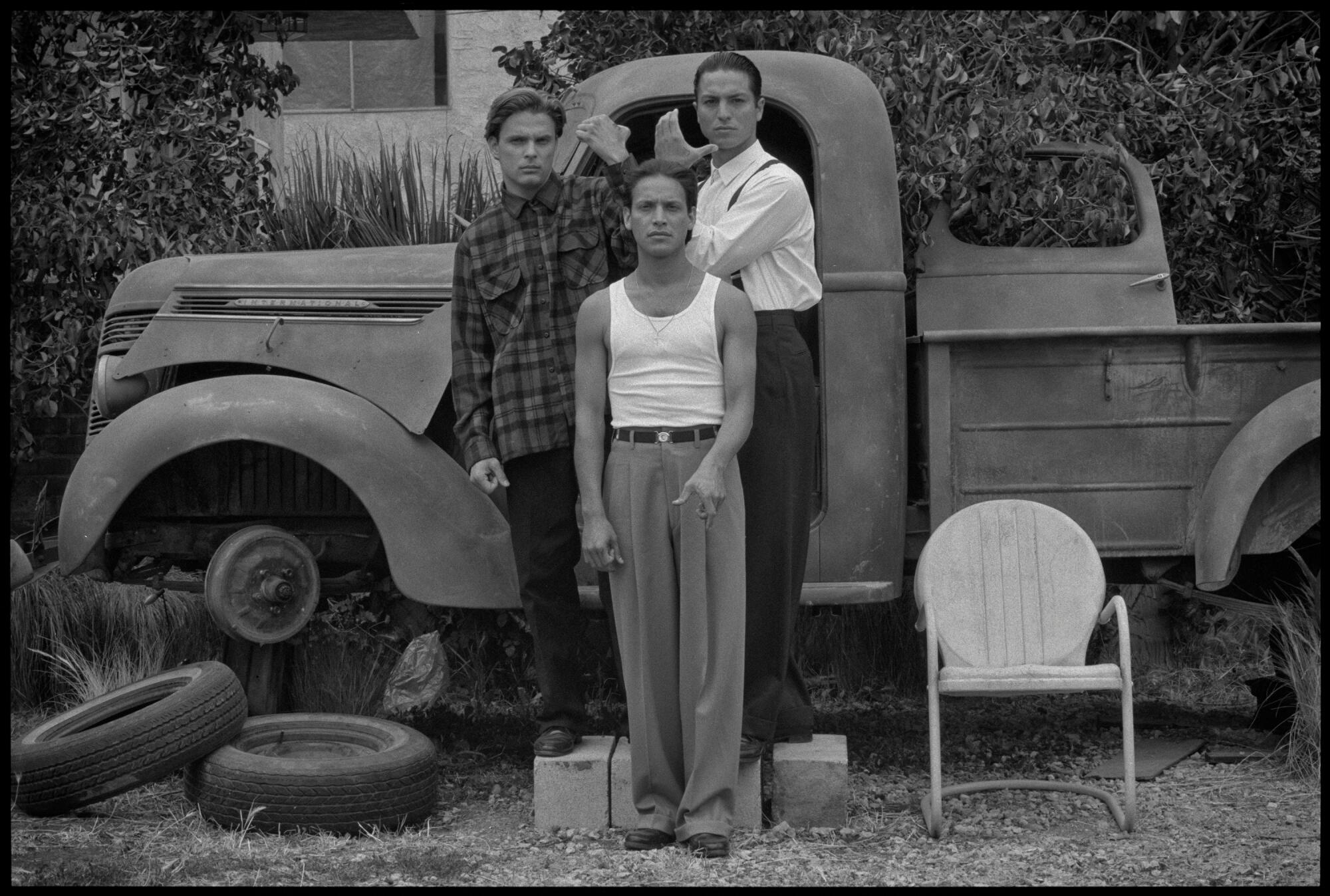 Black-and-white image of actors Damian Chapa, Jesse Borrego and Benjamin Bratt in front of a broken-down pickup truck.