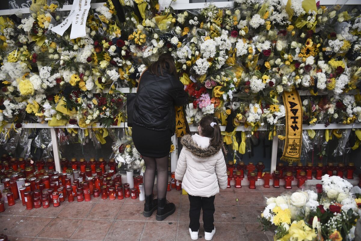 A woman places flower at the scene where a teenager was killed and two others injured after being stabbed outside the Aris FC stadium, in the northern port city of Thessaloniki, Greece, on Monday, Feb. 7, 2022. The victim was a fan of soccer club Aris, and his attackers were allegedly supporters of rival PAOK. Authorities in Greece have promised to toughen rules governing soccer supporters' associations in the wake of a deadly attack last week the left a 19-year-old man dead after he was stabbed and severely beaten in the northern city of Thessaloniki. (AP Photo/Giannis Papanikos)