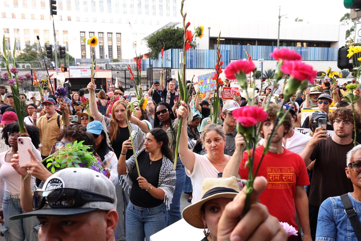 Hundreds of people, many holding flowers, march through downtown Los Angeles.