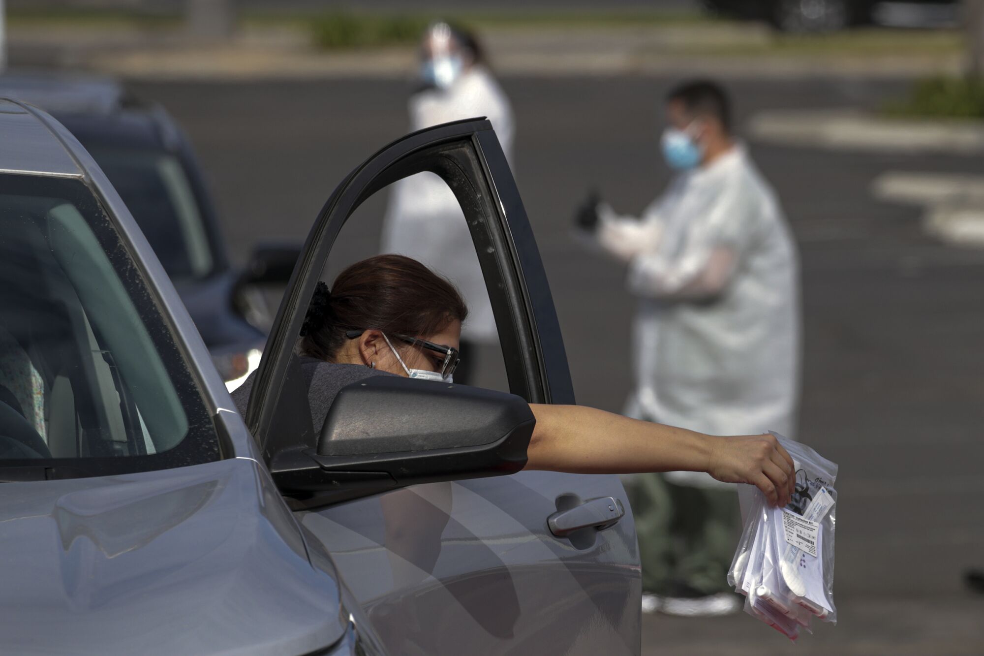 A motorist leans out the window of her open car door to deposit several plastic bags with test swabs.