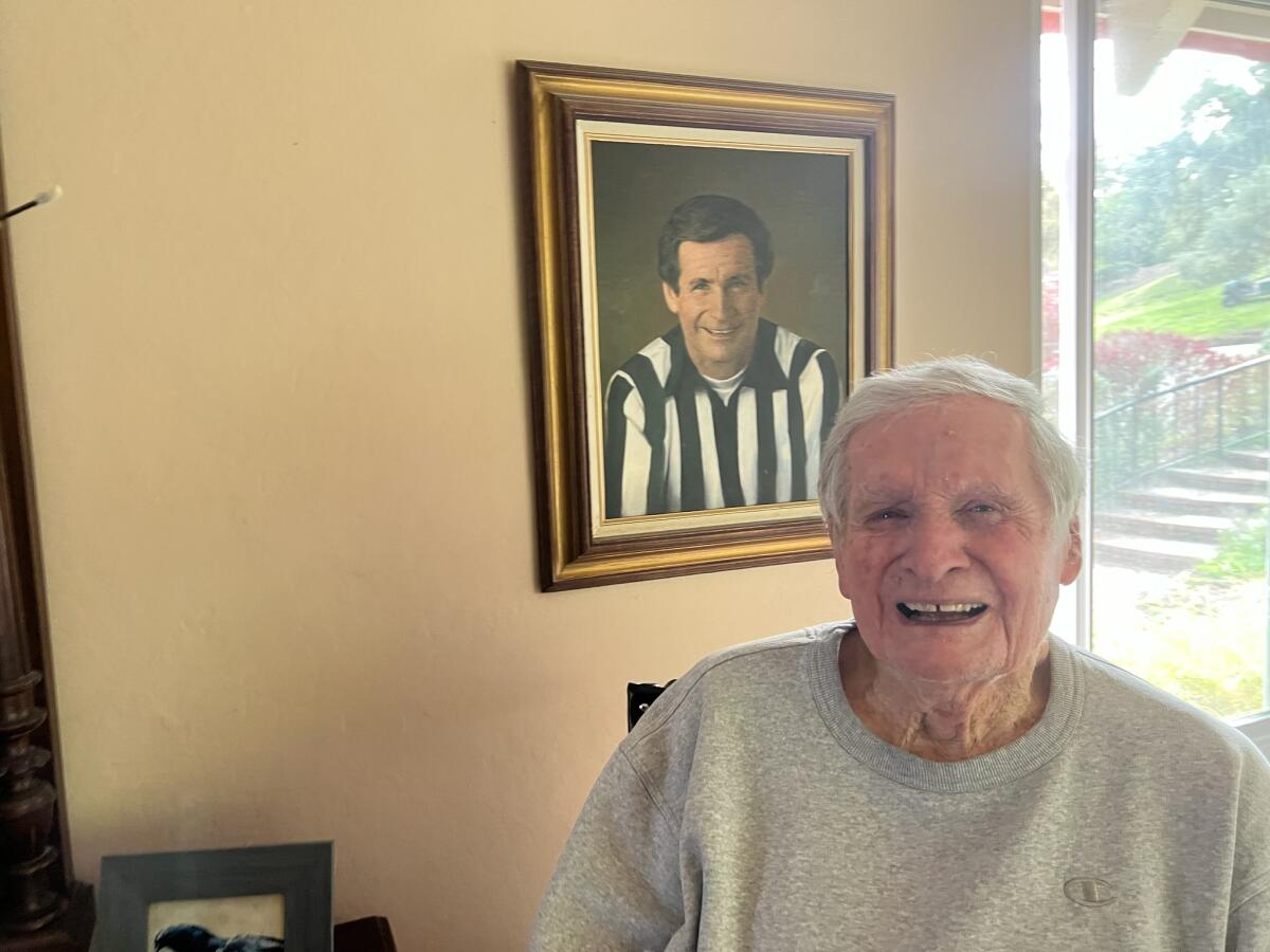 Former NFL referee Jim Tunney sits in front of a portrait of himself in a referee shirt at home.