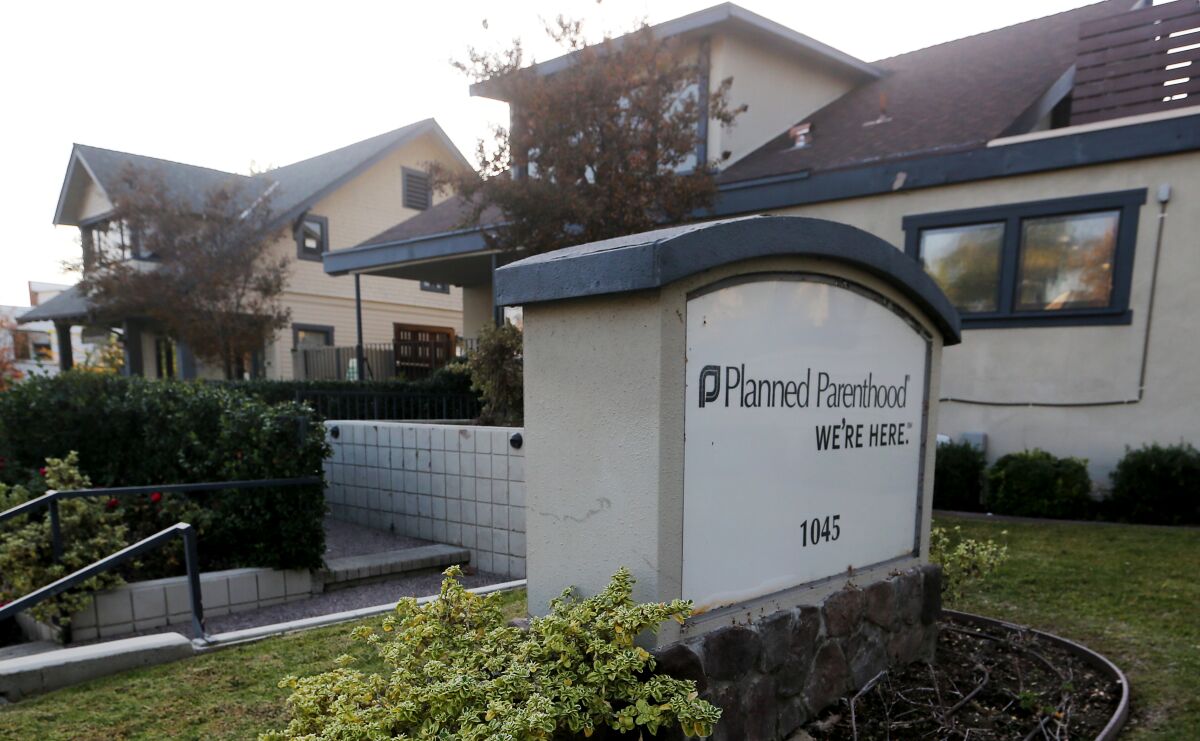 A sign in front of a building says "Planned Parenthood. We're Here."