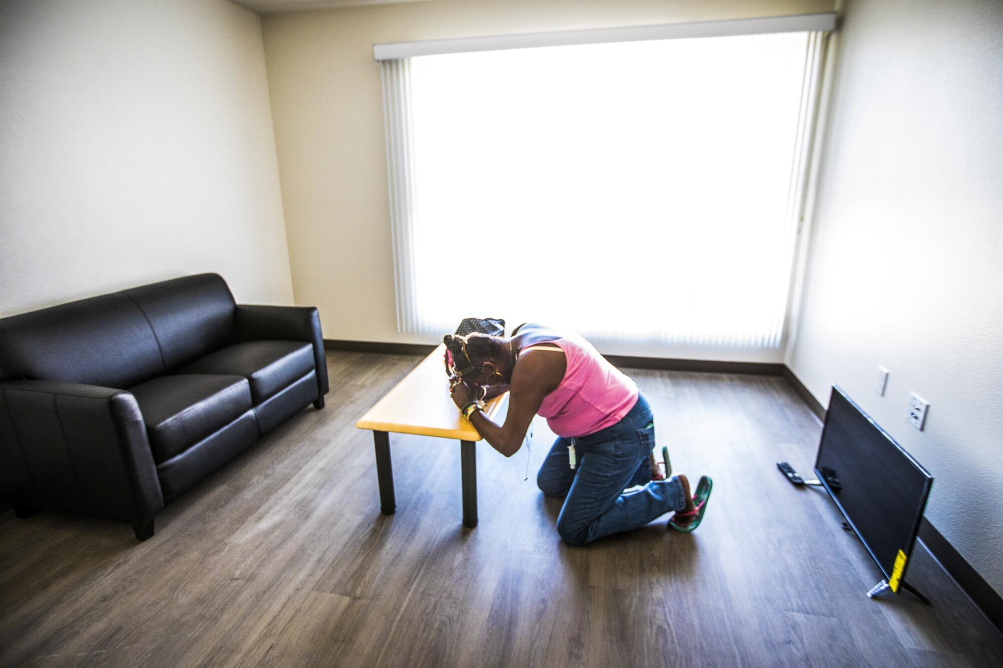 A woman prays inside a sparsely furnished apartment