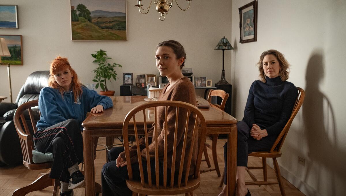 Three women sit at a living room table.