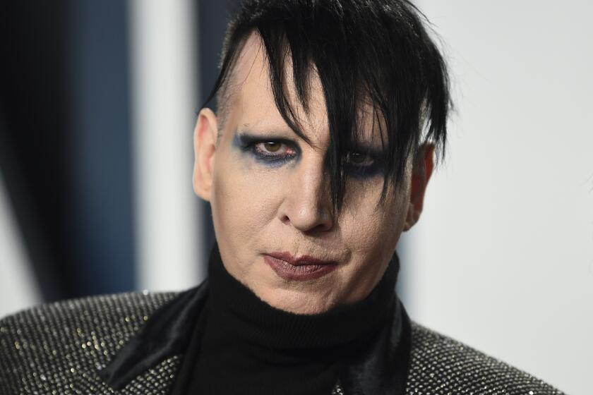 Marilyn Manson wears smeared makeup and a sparkly, turtleneck outfit.