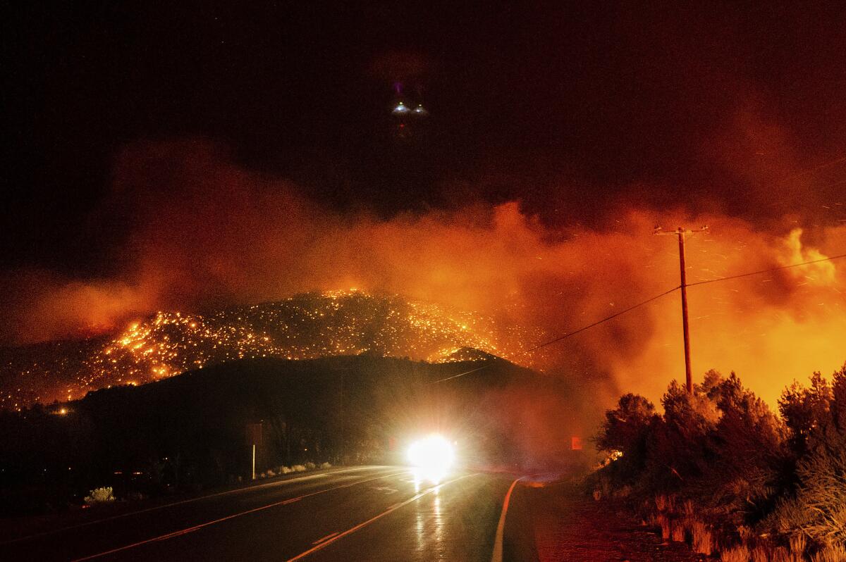 Un automóvil avanza por la autopista 395 en el condado de Mono mientras el incendio de Mountain View arde en el fondo.