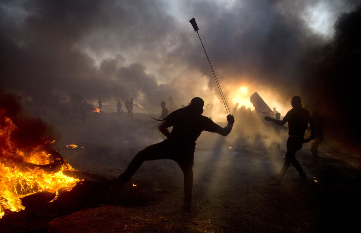 FILE- Black smoke from burning tires hangs in the sky as Palestinian protesters hurl stones toward Israeli troops during a protest at the Gaza Strip's border with Israel, Friday, Oct. 12, 2018. Rights groups said Thursday. Dec. 2, 2021, that Israel failed to investigate shootings that killed more than 200 Palestinians and wounded thousands at violent protests along the Gaza frontier in recent years, strengthening the case for the International Criminal Court to intervene. (AP Photo/Khalil Hamra, File)