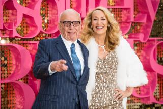 An elderly man with glasses and a suit poses for pictures alongside a blonde woman in a sparkling gown and a white coat. 