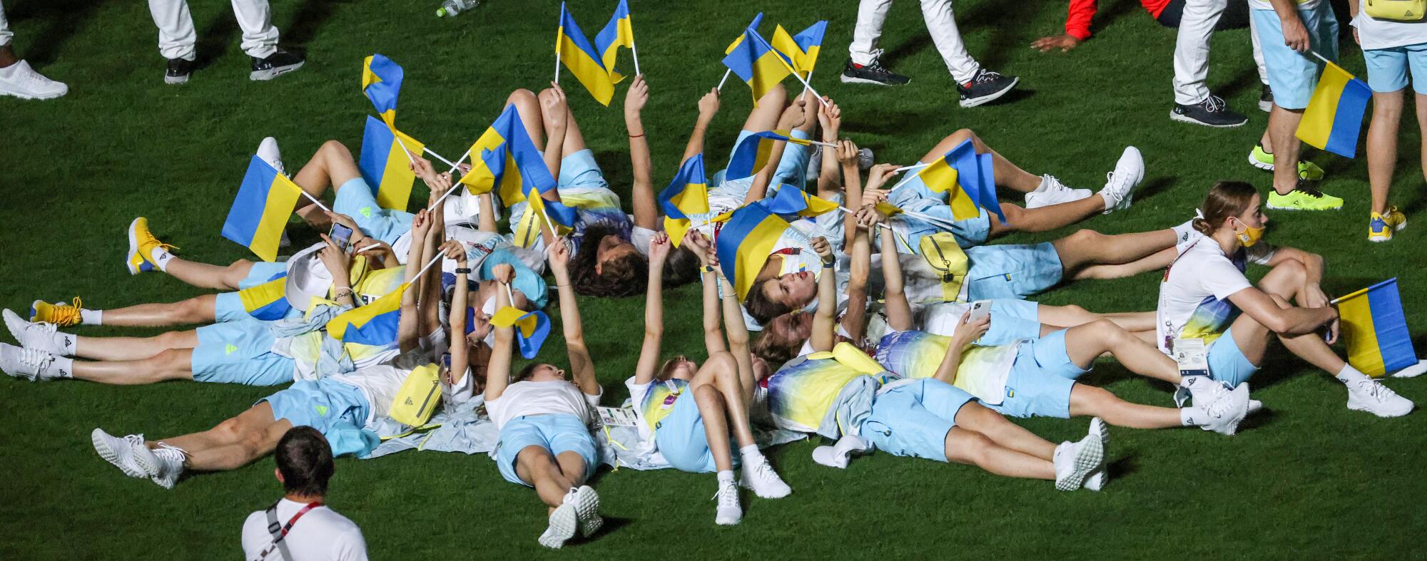 Young people lie in a circle with their heads in the center, waving small blue and yell flags.