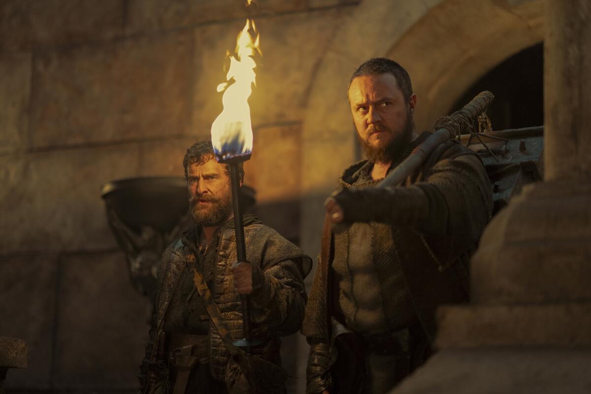 a bearded man holding a torch and another bearded man holding a rat cage