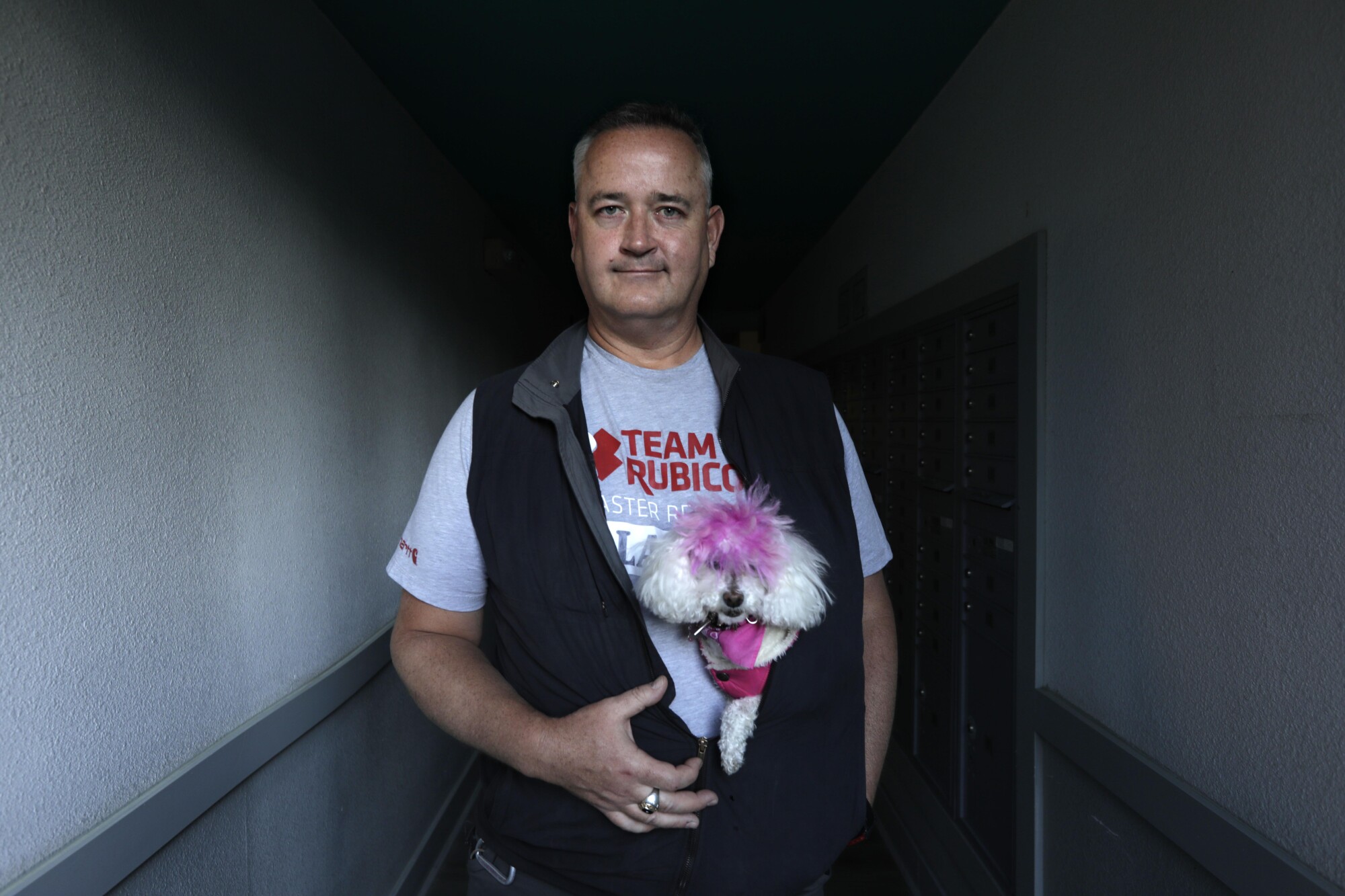 A man standing in a hallway with his toy poodle snuggled into his vest