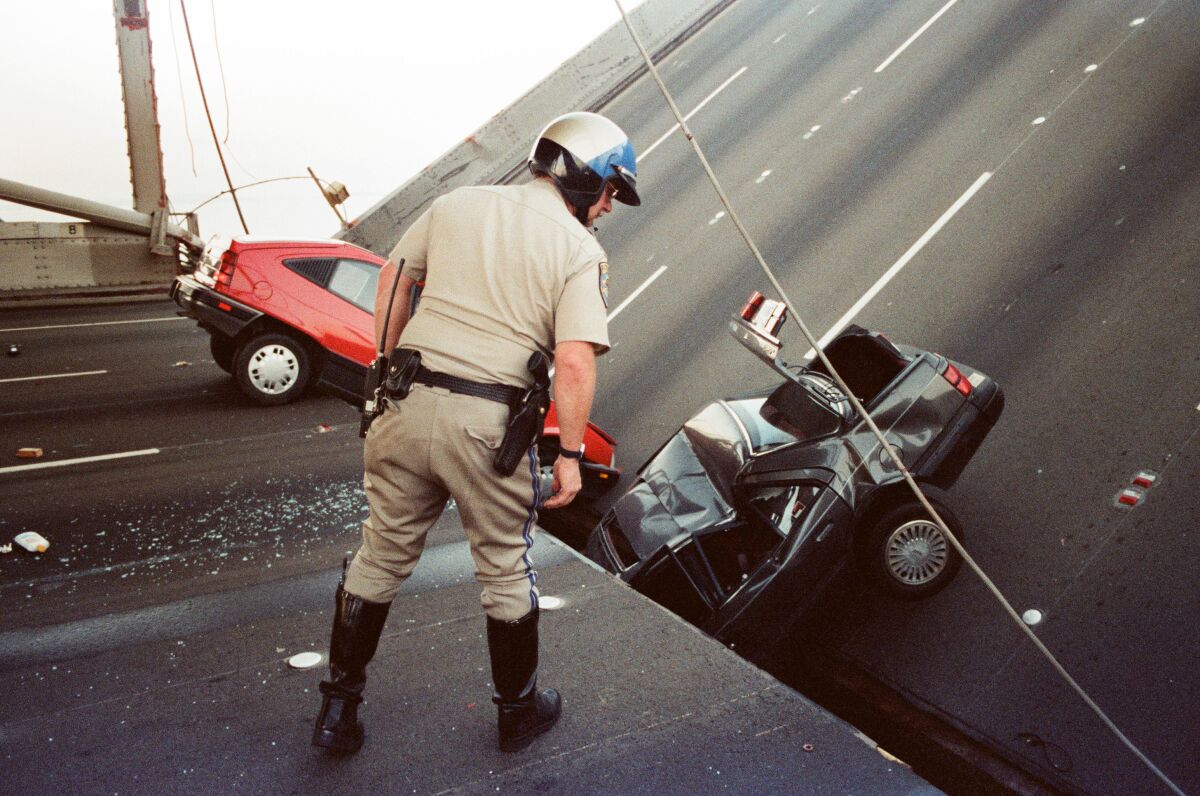 Law enforcement officer looks at damaged cars next to a bridge collapse