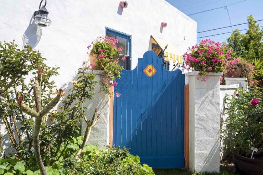 A blue gate adorns the entrance to a garden with potted plants at an adobe-style home.