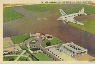 A TWA plane flies over airport buildings and runways.