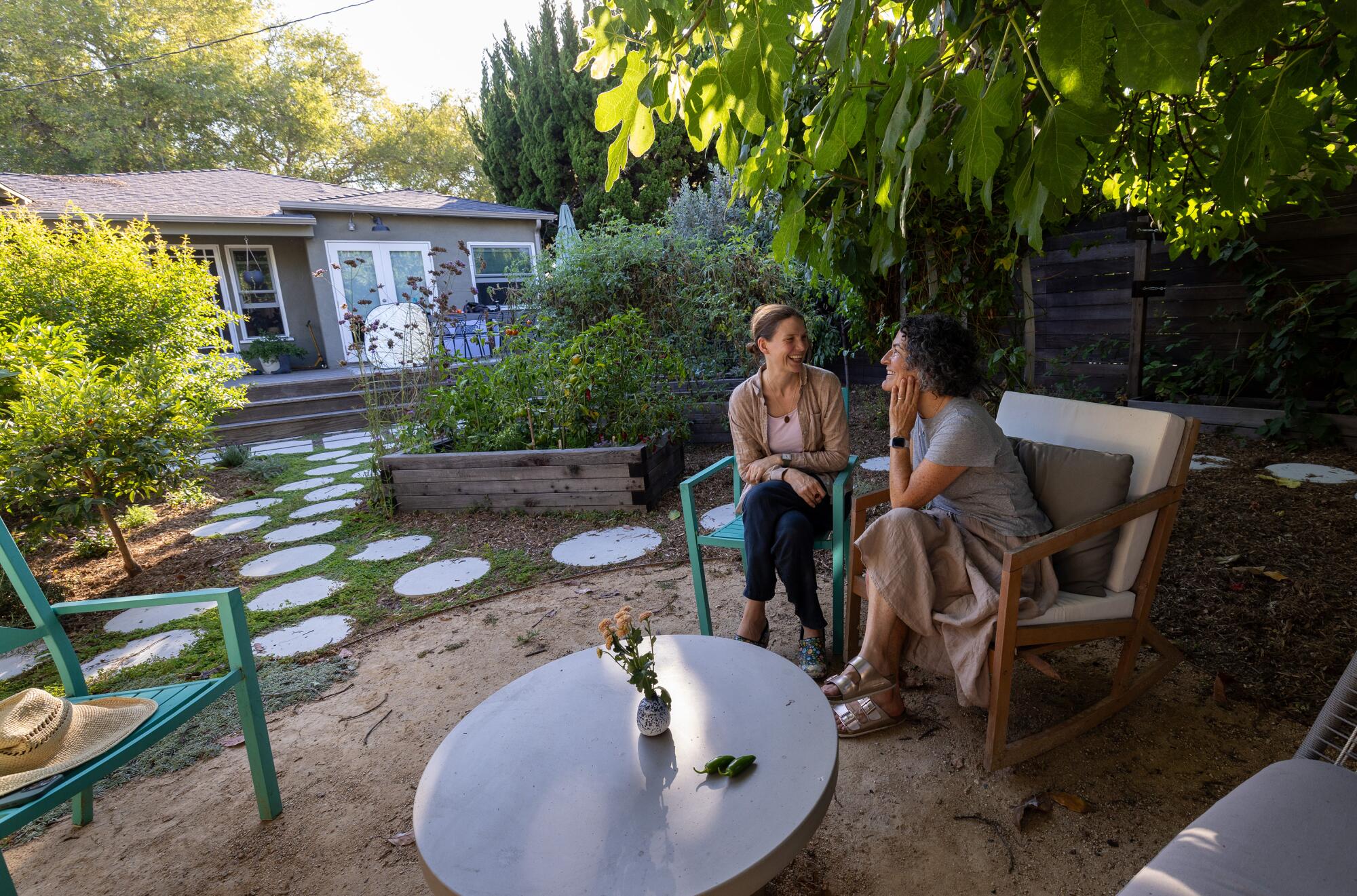 Dos mujeres, Catherine McLaughlin, izquierda, y Angel Black, están sentadas charlando alegremente en un exuberante jardín trasero.