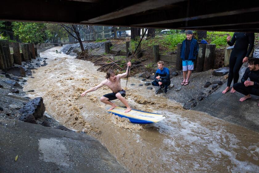A man takes his turn using a rope from a footbridge to stay in position and surf storm water.