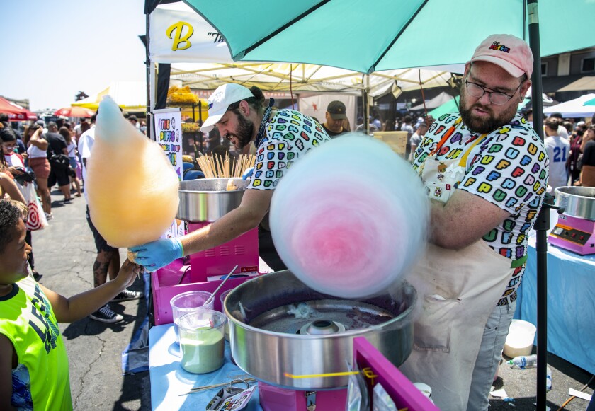 Two men prepare cotton candy at an outdoor food market