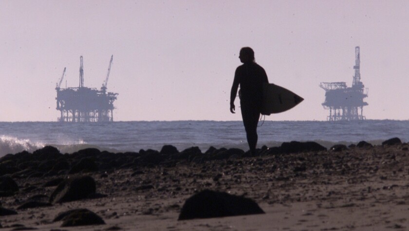 A rider watches the waves off the northern Ventura County coast along the Rincon Beach area with two oil rigs in the distance.