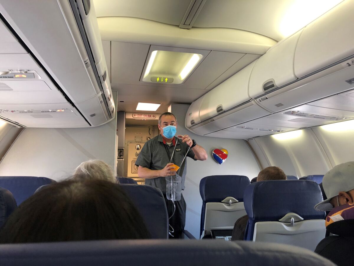 A flight attendant, wearing a face mask, demonstrates the use of an oxygen mask.