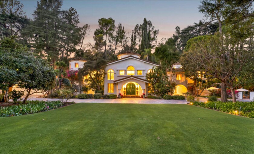 A grassy lawn leads to a large, well-lighted Mediterranean-style house.