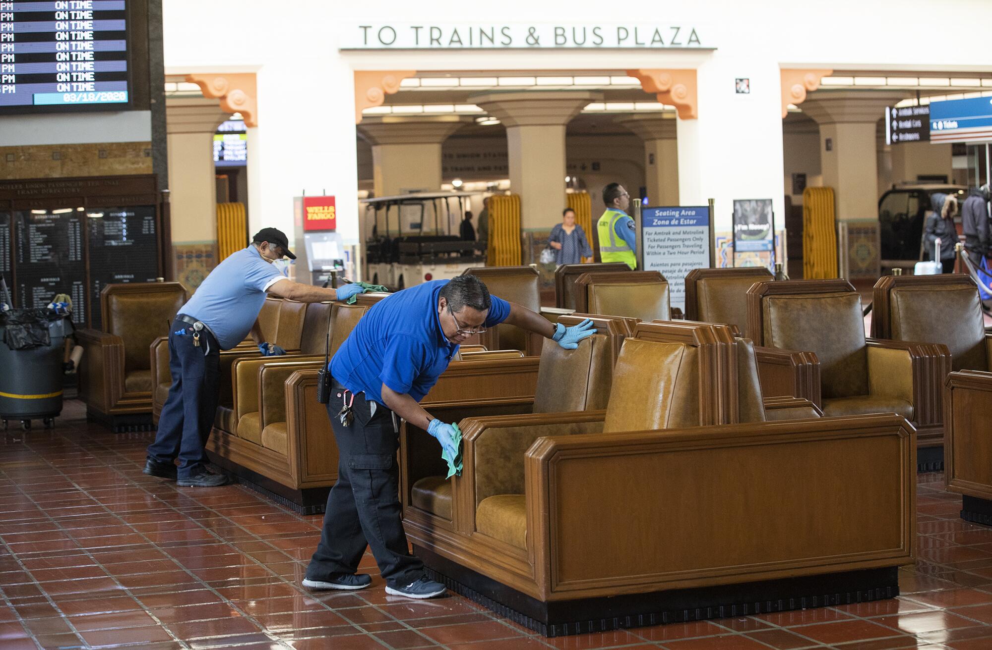 Salvador Lareas, left, and Raul Arias clean chairs with disinfectant inside Union Station in downtown Los Angeles. 