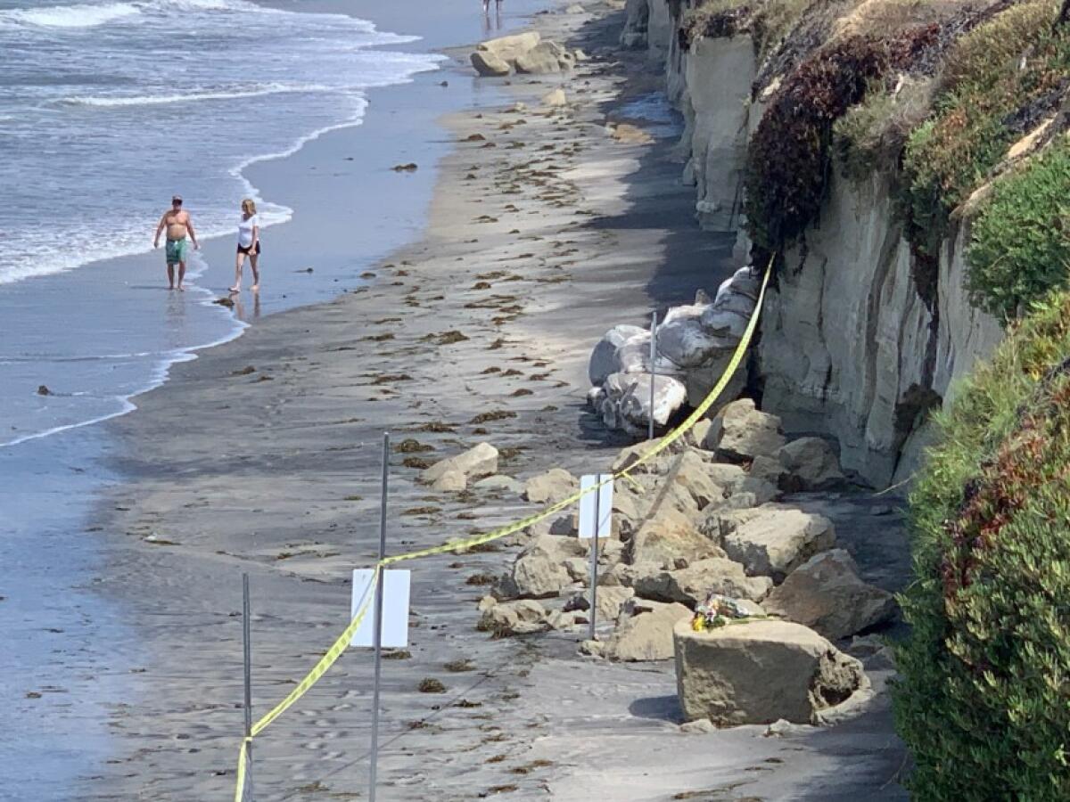 People walk near the site of a deadly bluff collapse in August at Grandview Beach in Encinitas. Three people on the narrow beach died when a large chunk of sandstone slid off the cliff.