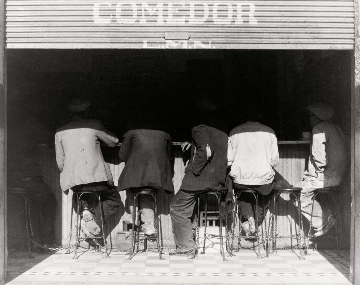 A black-and-white image of people seated on stools at a counter, seen from behind
