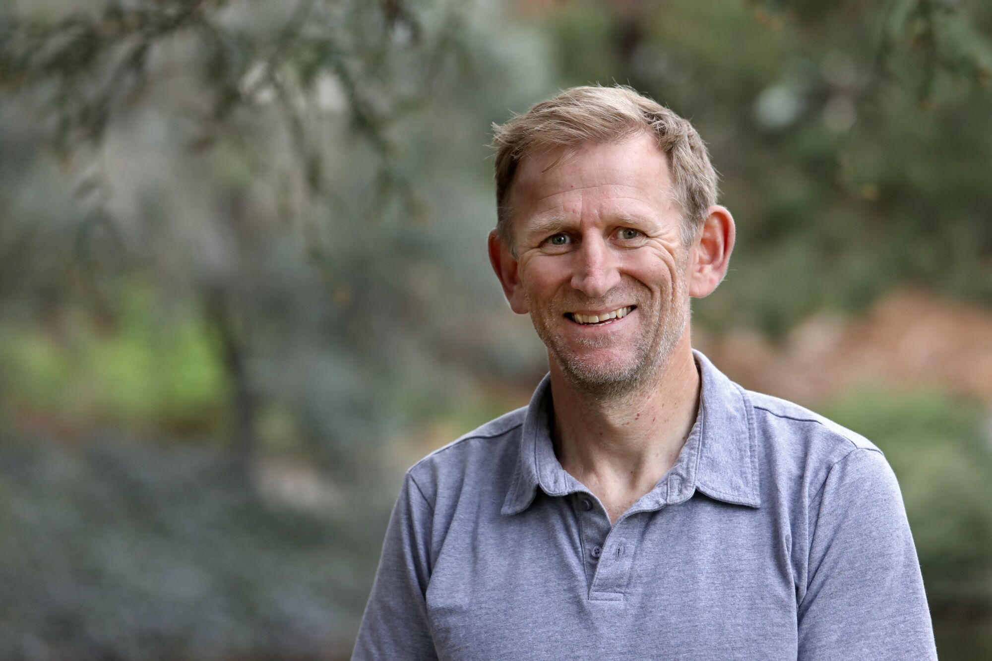 UC Davis professor Aaron Smith smiles as he stands near greenery.