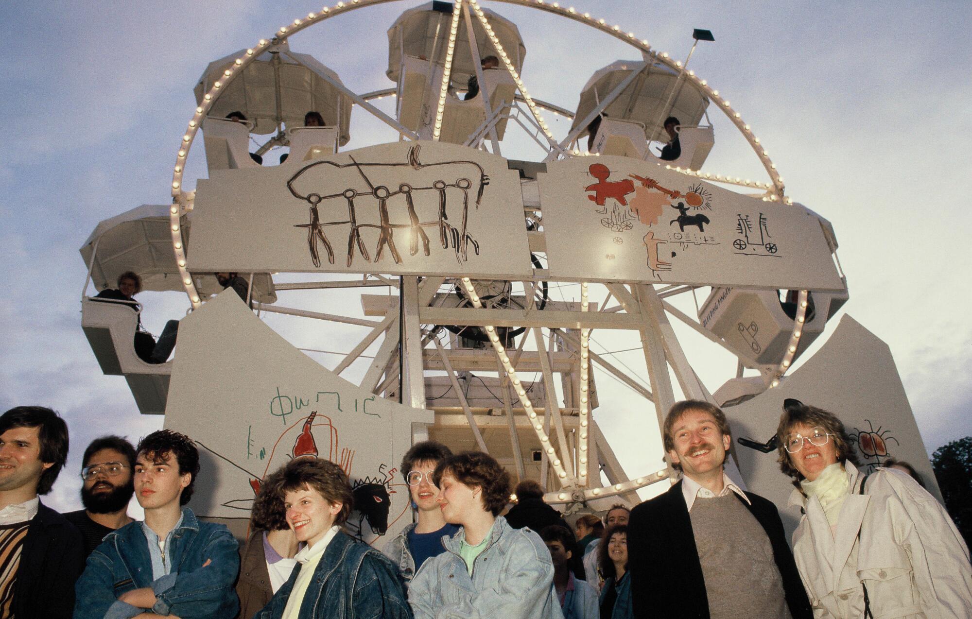  People on the ground in front of Jean-Michel Basquiat's Ferris wheel, which is adorned with the artist's sketches. 