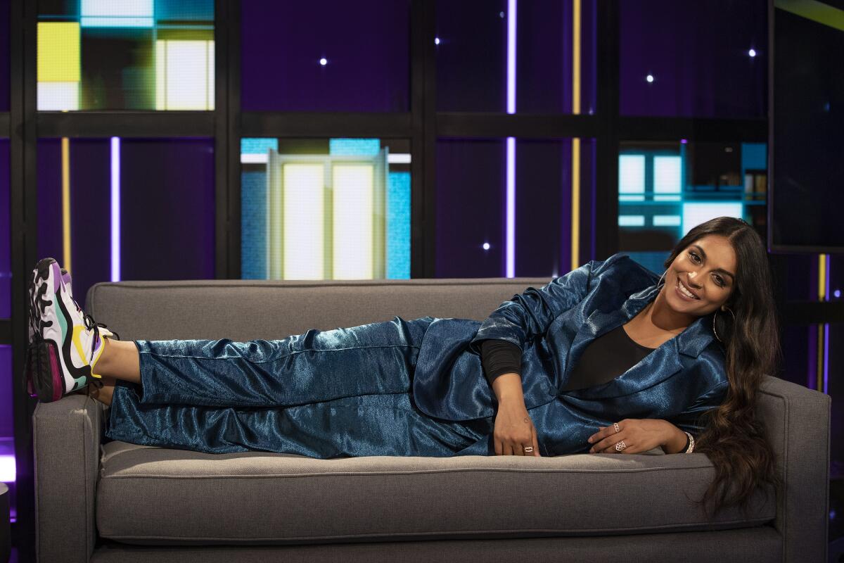 Lilly Singh laying on the couch on the set of her new show, "A Little Late"