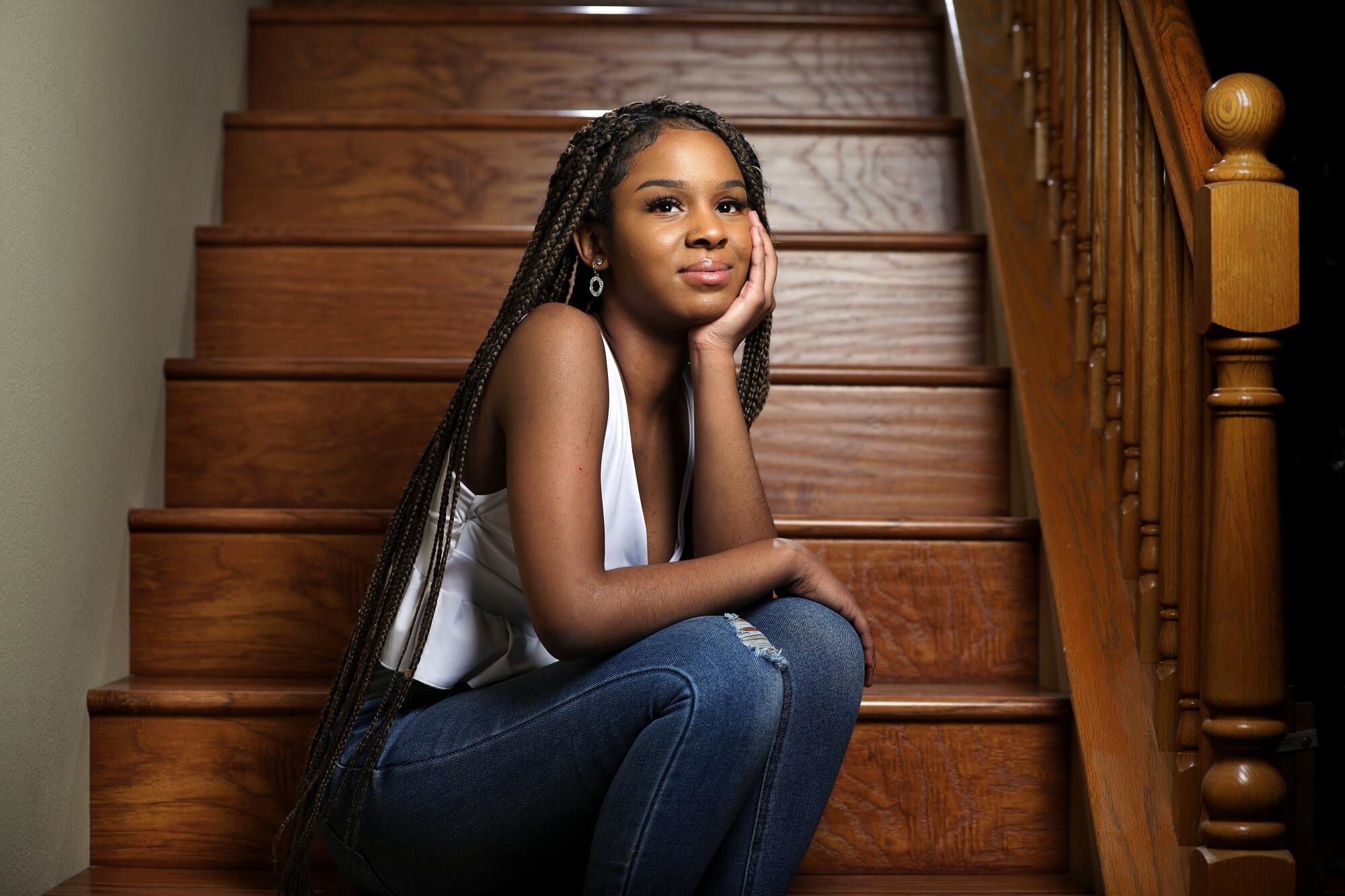 A young woman poses thoughtfully on hallway stairs.