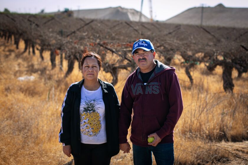 SELMA, CA - SEPTEMBER 29: Yesenia and Norberto Diaz stand in the driveway as their home as they are surrounded by a noisy bullet train construction site that installed high volume water wells, resulting in the family's domestic well to run dry on Wednesday, Sept. 29, 2021 in Selma, CA. (Jason Armond / Los Angeles Times)